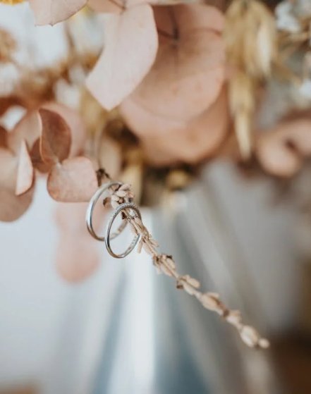 alianzas de boda colgando de un tallo de un ramo de flores color rosa palo